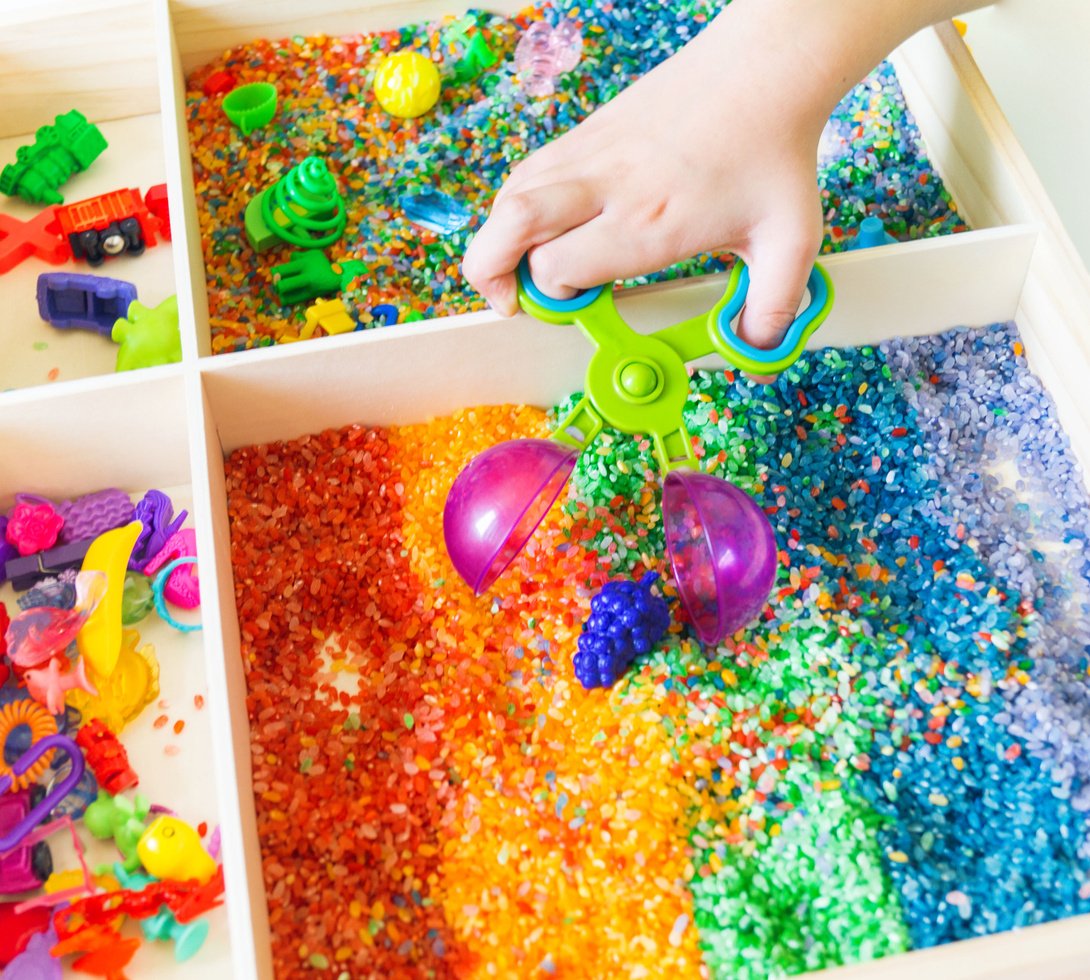 Sensory box with rainbow rice inside. Montessori material baby